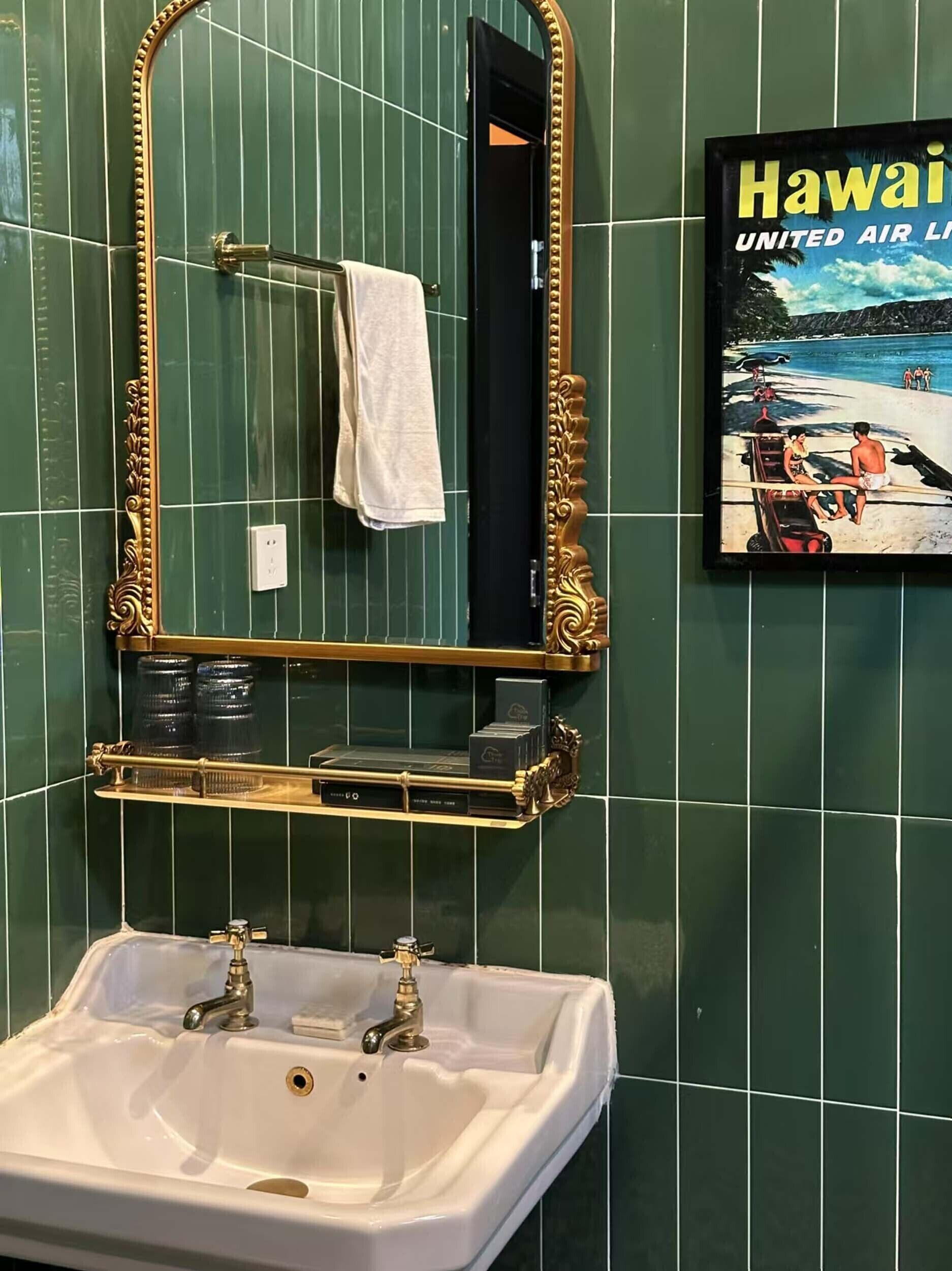 Een badkamer met een witte wastafel, een spiegel met gouden lijst en een foto van een strand.