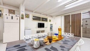 Eine Essecke mit einem Tisch für zwei Personen, einem Kühlschrank, einer Mikrowelle und einem Fernseher an der Wand.