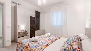 Ein modernes Hotelzimmer mit einem großen Bett, einem Nachttisch, einem Spiegel und einem Fenster mit durchsichtigen Vorhängen.