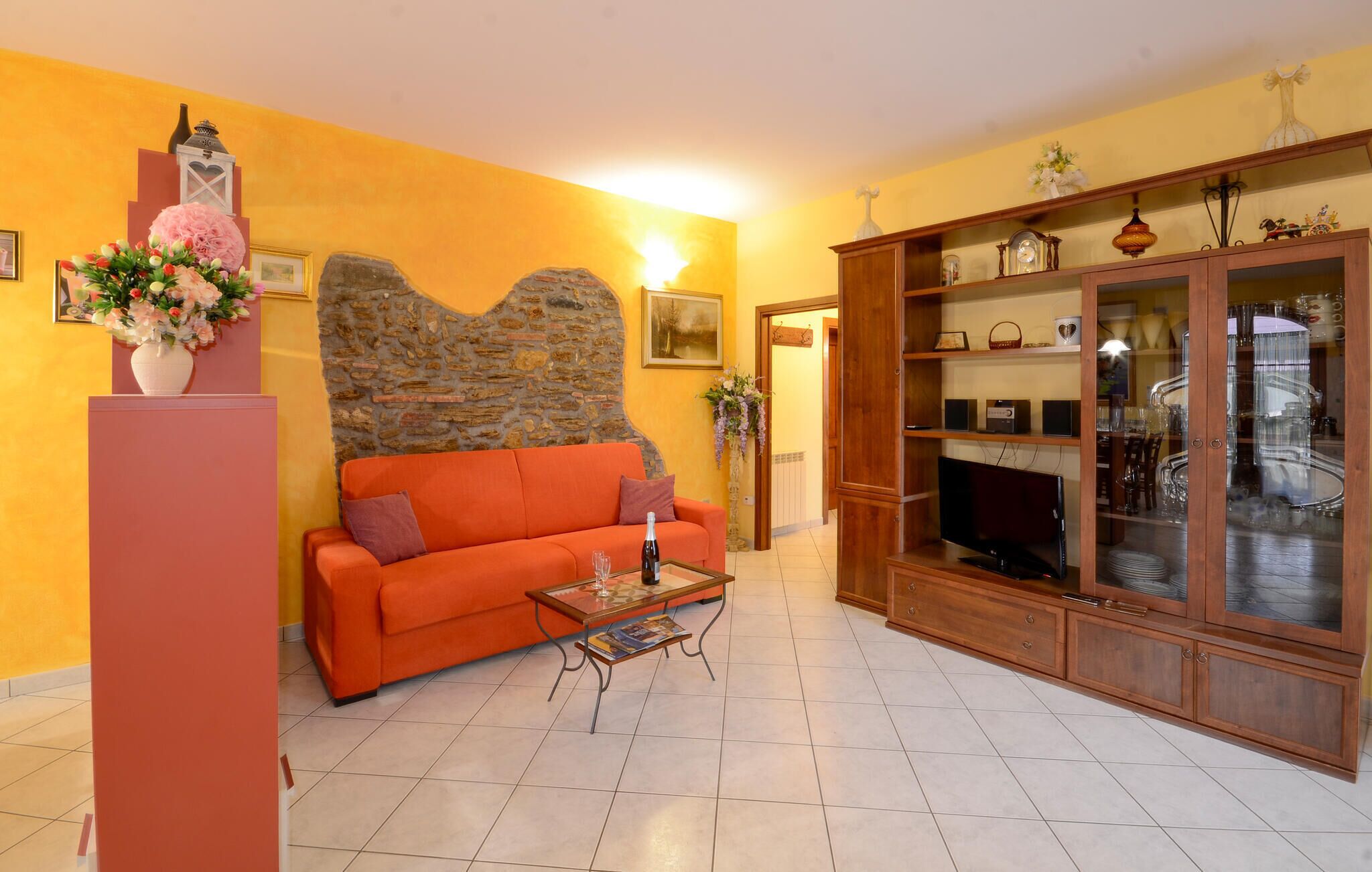 A living room with a stone wall, orange sofa, and wooden cabinet with glass doors.