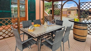 Un patio al aire libre con una mesa lista para comer, sillas de mimbre y un barril decorativo.