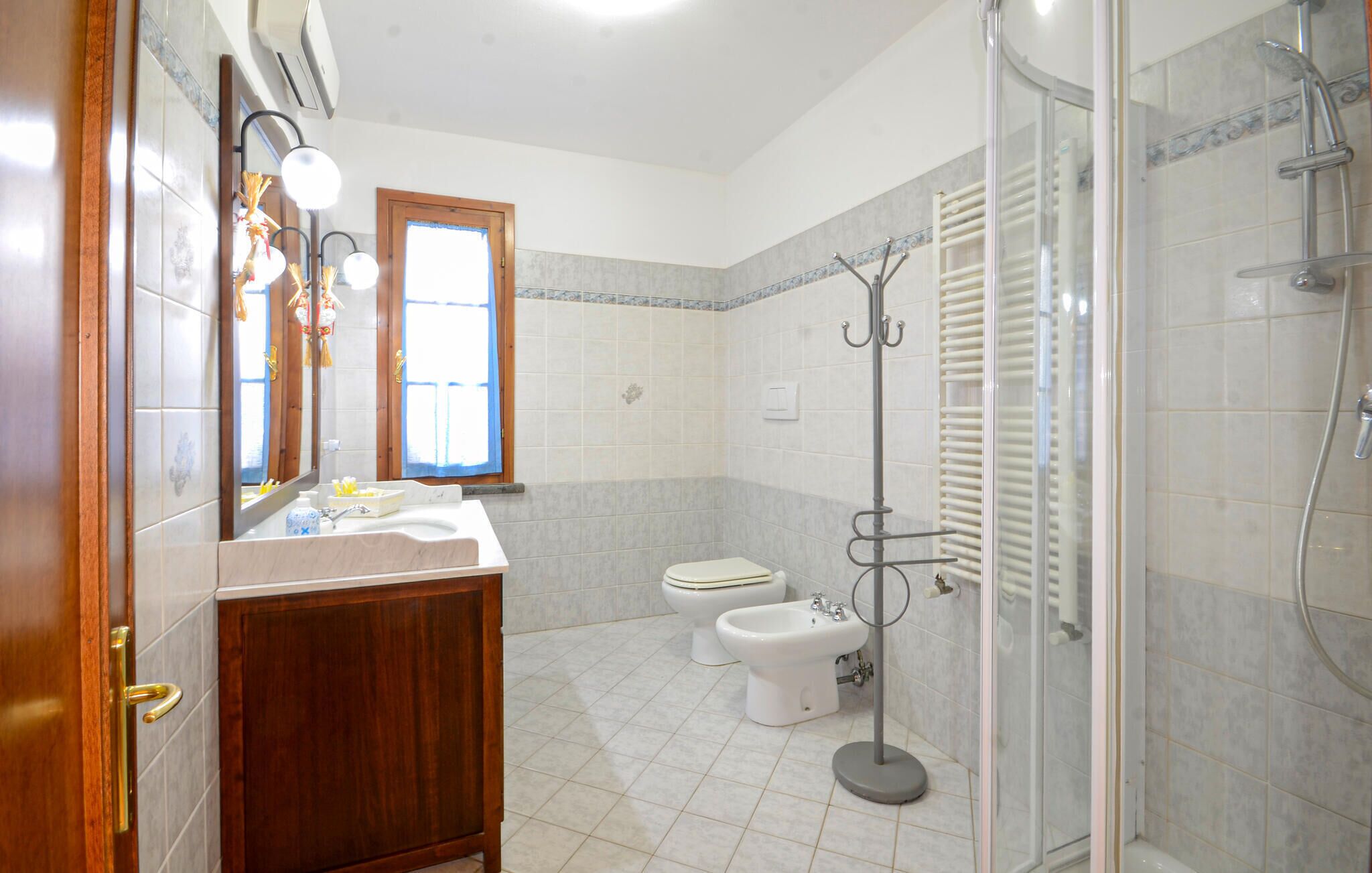 Une salle de bain avec un meuble-lavabo en bois, un évier, des toilettes, un bidet et une douche à parois de verre.