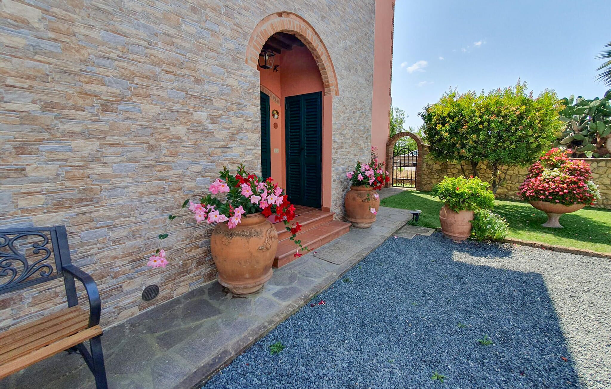 Un bâtiment en pierre avec un banc en pierre, une entrée pavée et de grands pots de fleurs.