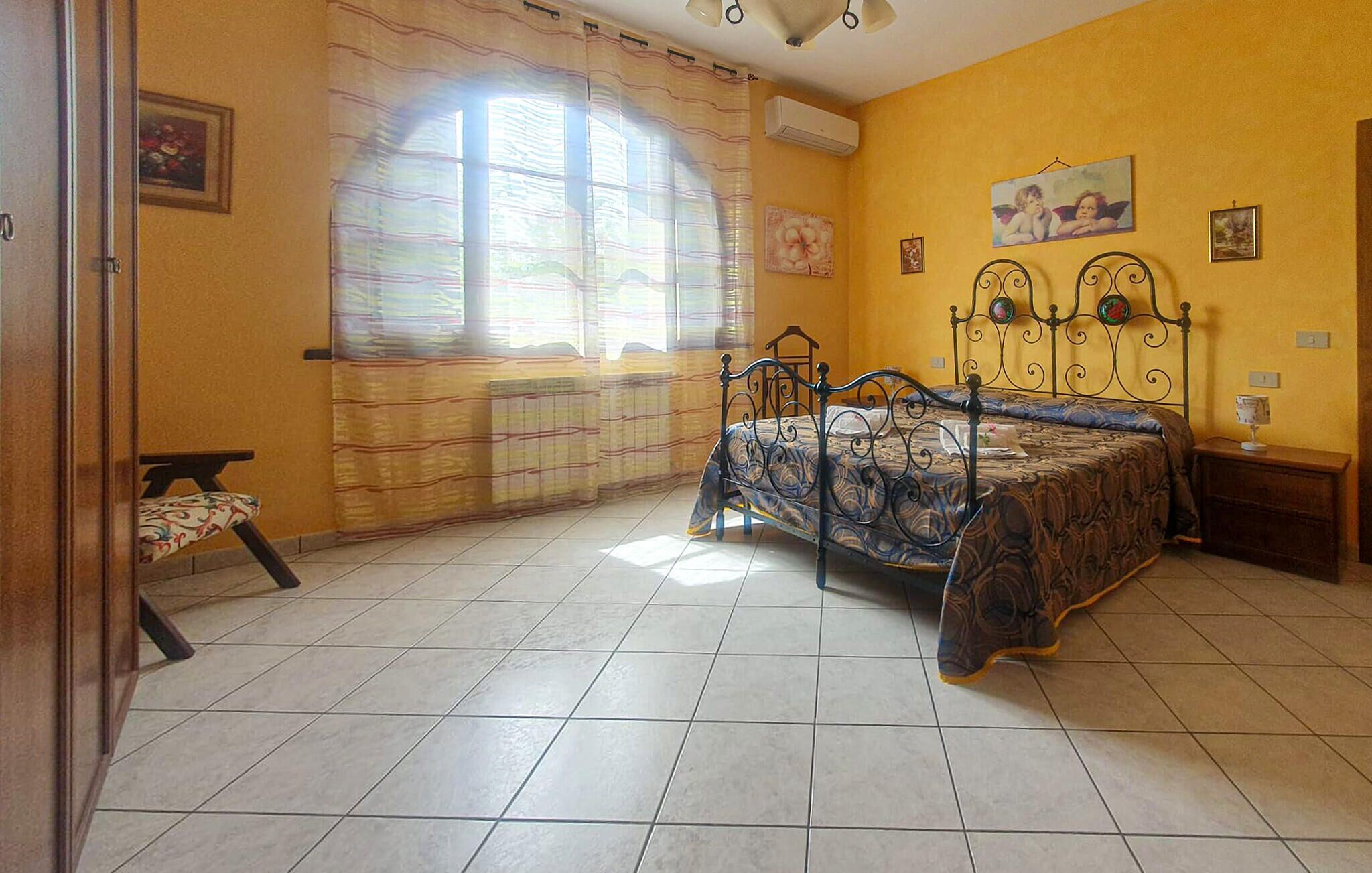 A bedroom with a bed, a chair, a nightstand, and a window with curtains.