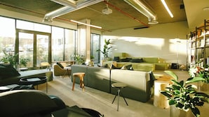 Un espacio de oficina moderno con un sofá verde, taburetes de madera y una estantería.