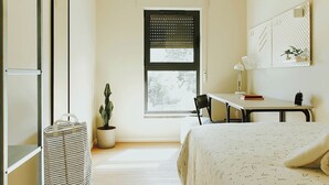Un dormitorio con cama, escritorio, silla, ventana y planta en maceta.