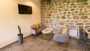 Un rincón tranquilo con paredes de piedra, un sofá, sillones, una mesita de centro y plantas colgantes.