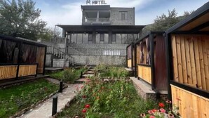 Un hotel con fachada de piedra, un balcón y un jardín lleno de flores rojas.