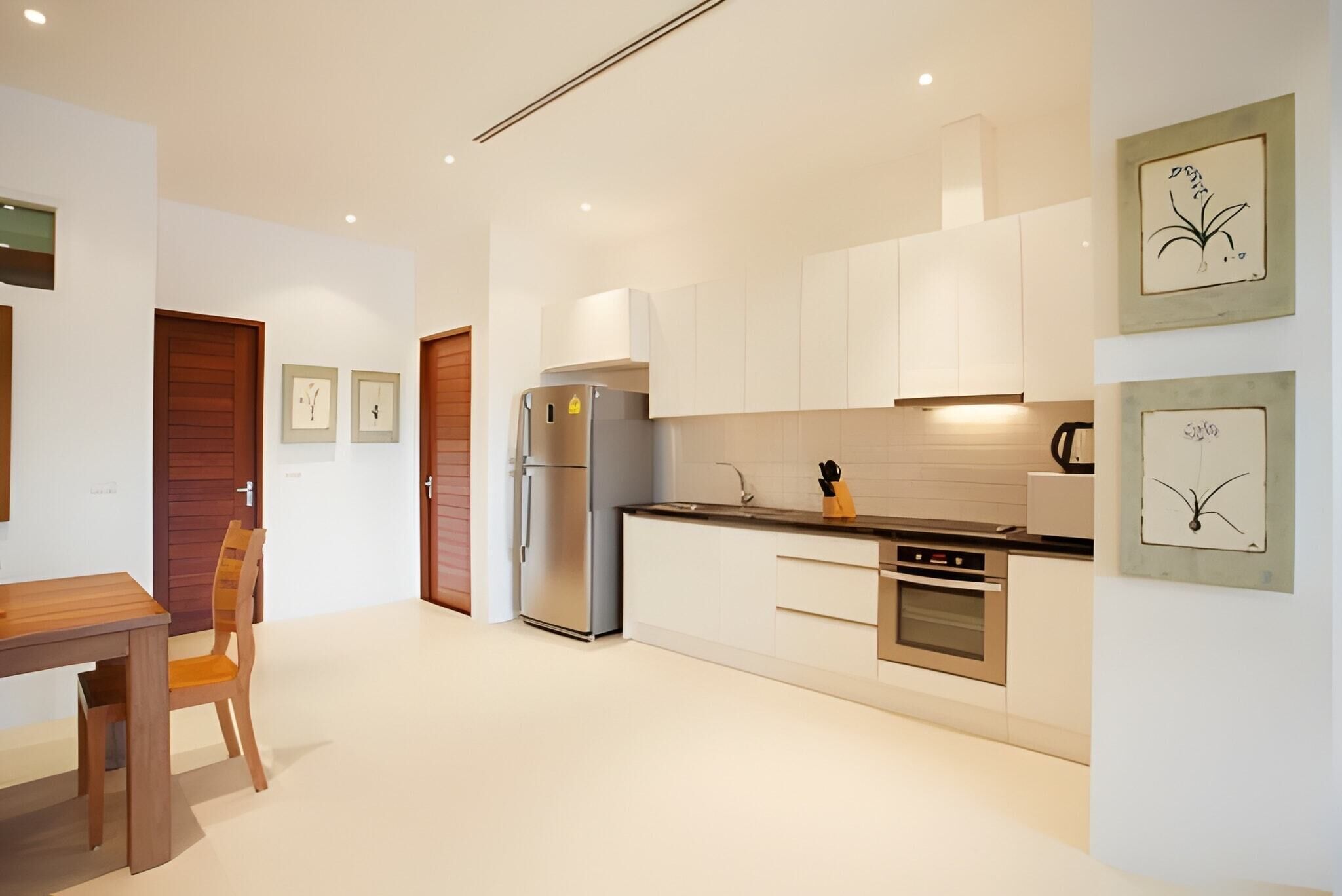 A modern kitchen with white cabinets, a stainless steel refrigerator, and a wooden dining table with a chair.