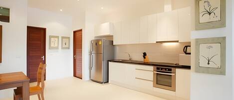 A modern kitchen with white cabinets, a stainless steel refrigerator, and a wooden dining table with a chair.