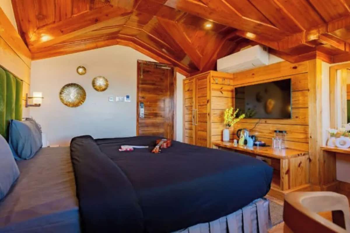 A cozy room with a bed, a wooden ceiling, a TV, and a small table with a vase of flowers.