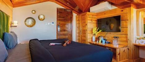 A cozy room with a bed, a wooden ceiling, a TV, and a small table with a vase of flowers.
