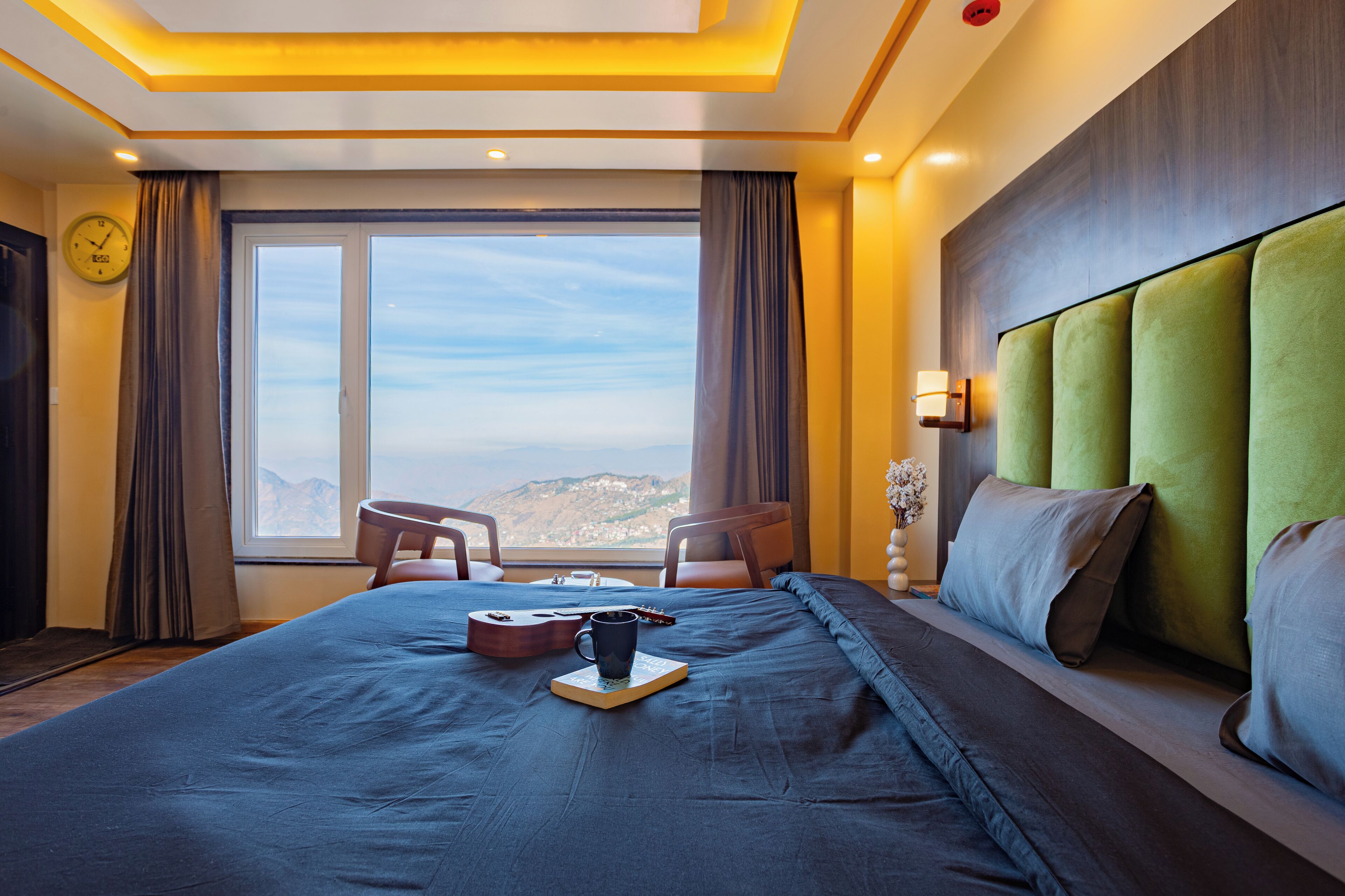 Habitación de hotel con una cama grande, vistas a las montañas, un reloj en la pared y una ventana con cortinas.