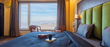 Habitación de hotel con una cama grande, vistas a las montañas, un reloj en la pared y una ventana con cortinas.