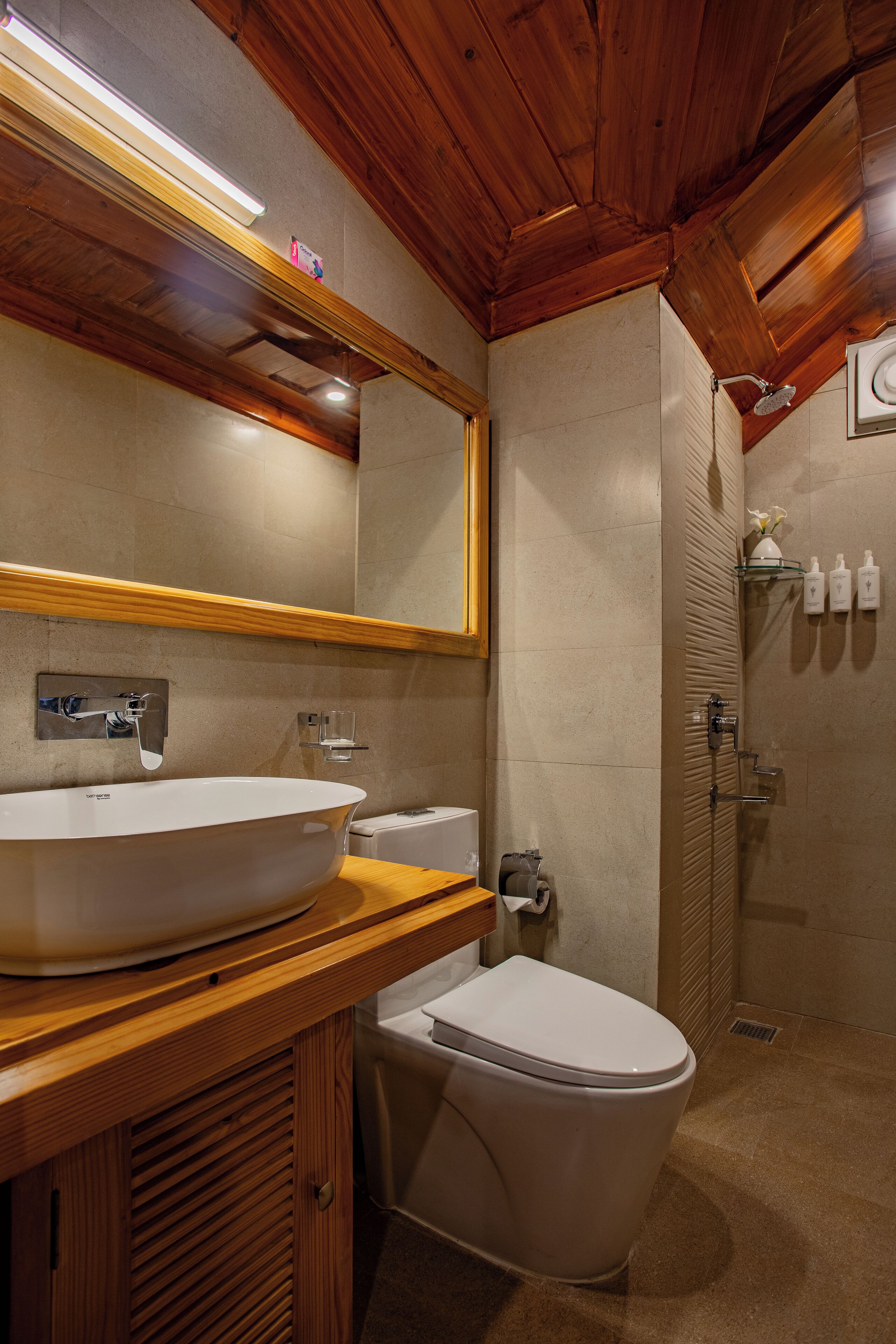 A bathroom with a wooden vanity, a large oval sink, a toilet, and a shower area.