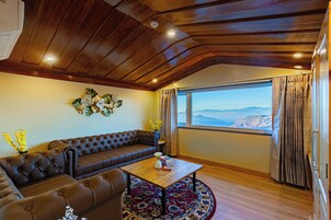Una habitación con un sofá de cuero marrón, una mesita de centro de madera y un amplio ventanal con cortinas.
