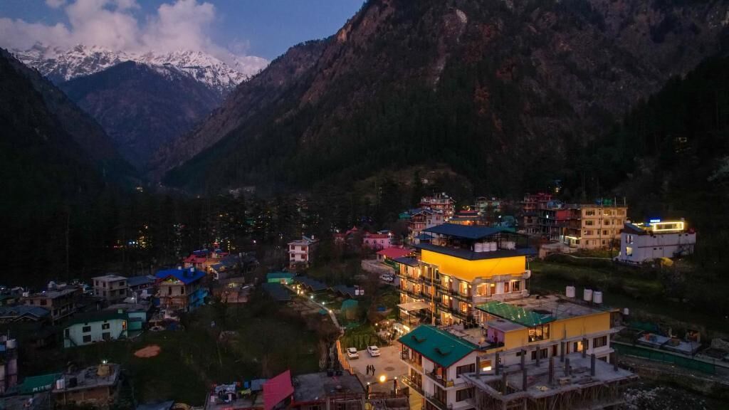 A mountainous town with buildings, including a brightly lit hotel with multiple floors and balconies, surrounded by snow-capped mountains.