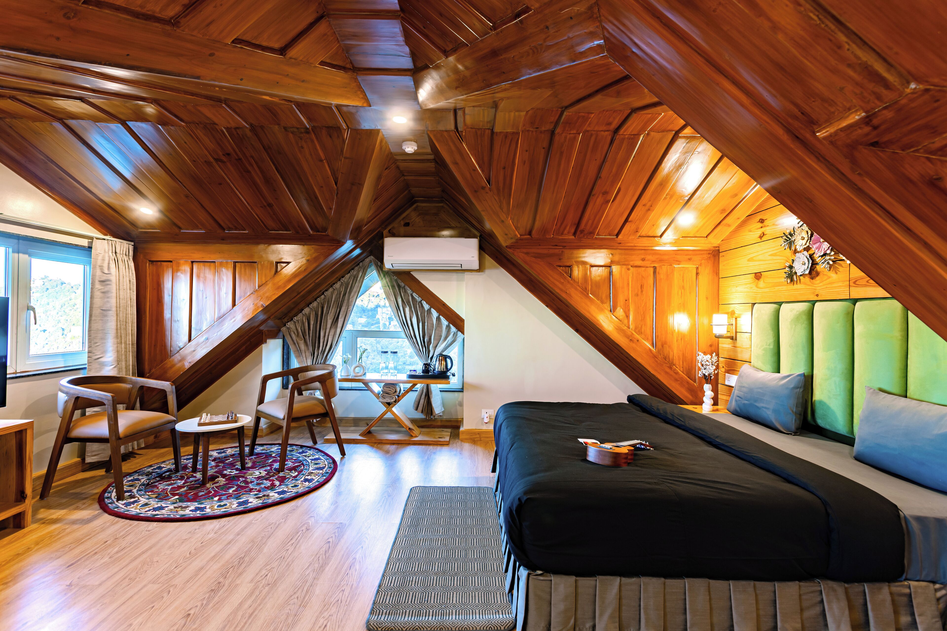 A cozy attic bedroom with a bed, seating area, and a view of the outdoors.