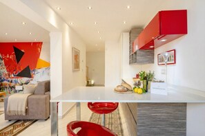 A modern kitchen with a white countertop, red accents, and a colorful abstract painting on the wall. - Lemon Tree House – Simple, Bright, and Peaceful (Bari)