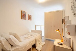 A bedroom with a bed, a bedside table with a lamp, a wardrobe, and a small shelf with books. - Lemon Tree House – Simple, Bright, and Peaceful (Bari)