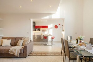 A modern living room with a brown sofa, a dining table set for four, and a kitchen in the background with red accents. - Lemon Tree House Simple and Peaceful (Bari)
