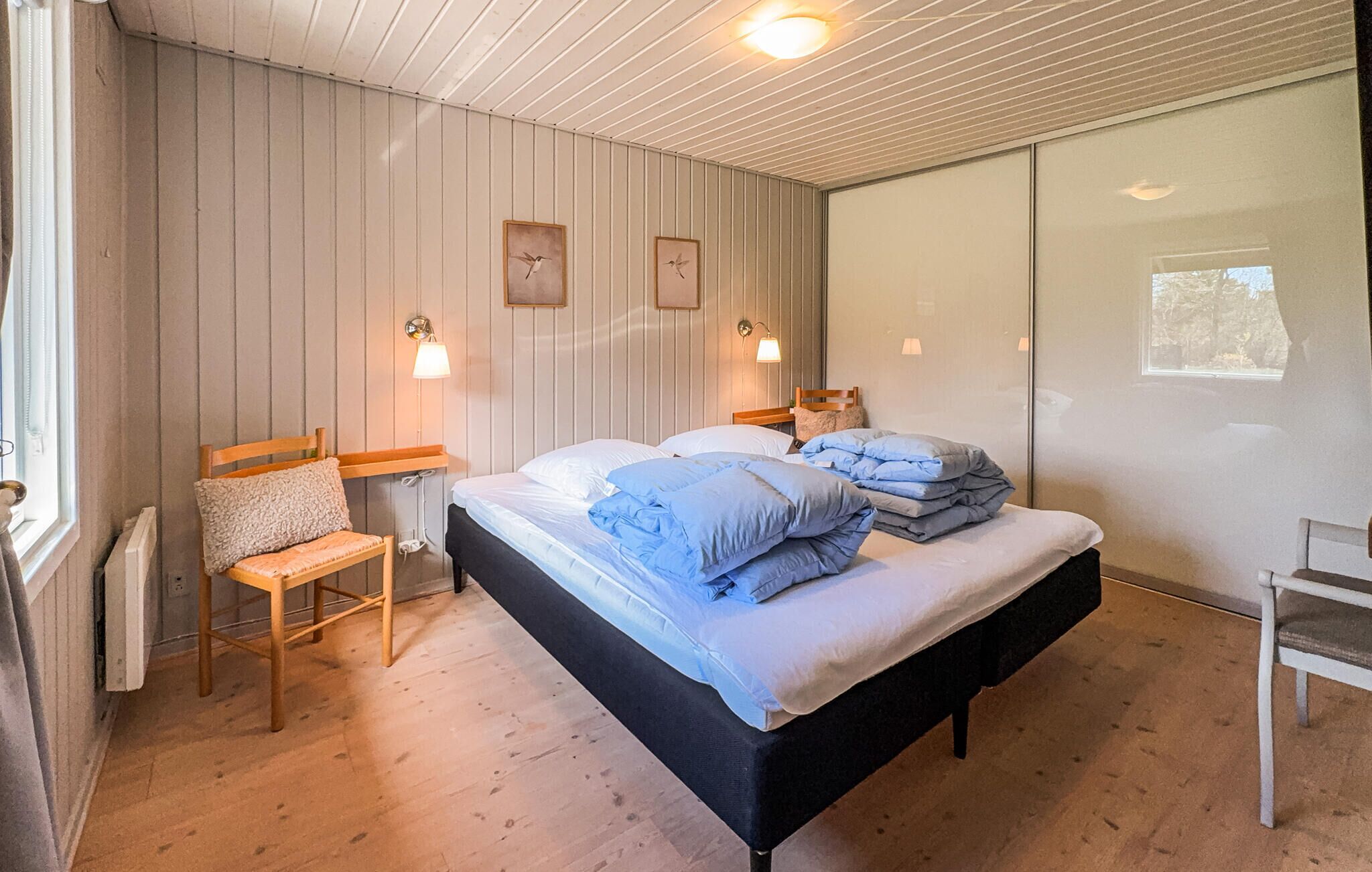 Quarto com cama, duas mesas de cabeceira, uma cadeira, uma janela e parede com duas fotos emolduradas.
