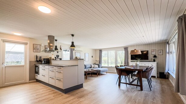 A modern kitchen with a central island, a dining area with a wooden table and chairs, and a large window providing natural light.