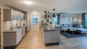 A modern kitchen with a central island, a dining area with a sofa, and a view through a door.