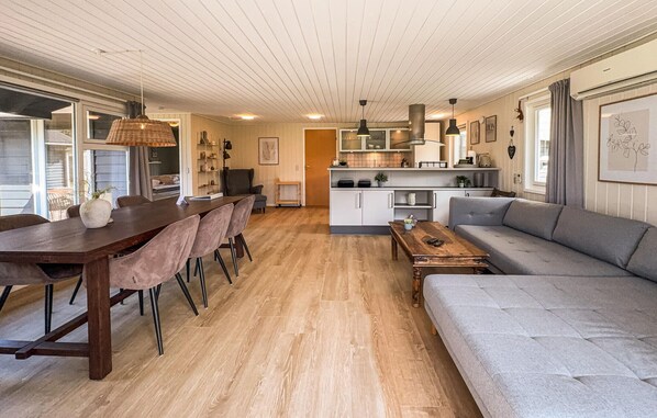 Un vaste espace de vie comprenant une table à manger en bois, un canapé gris et une cuisine à l’arrière-plan.
