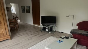 Una sala de estar con televisión, una mesa de centro y un sofá rojo.