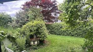 Un jardín con seto, una estatua y una silla de metal blanca.