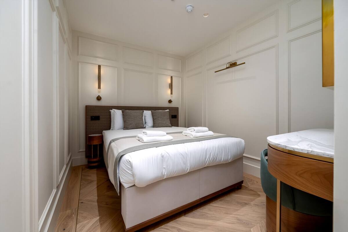 A hotel room with a large bed, bedside lamps, a wooden floor, and a marble-topped vanity.