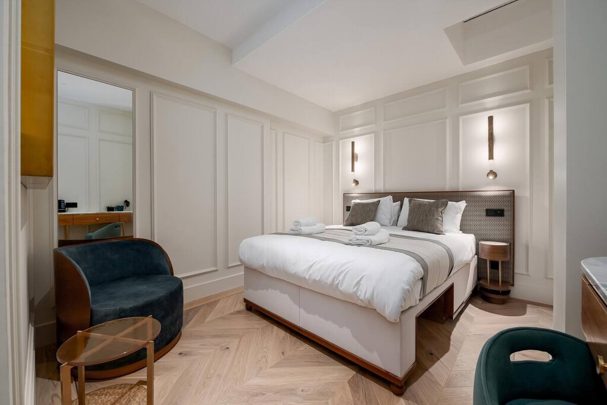 A modern bedroom with a large bed, a curved armchair, a small table, and a bedside lamp.