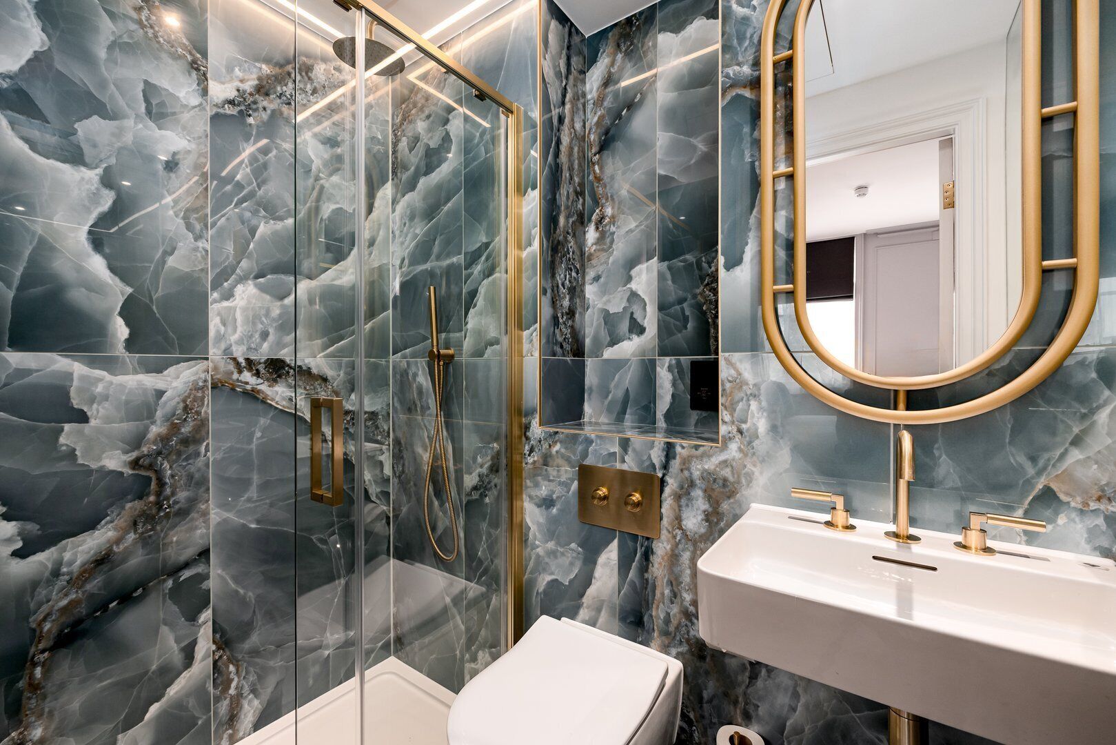 Un baño moderno con paredes de mármol, cabina de ducha con vidrio y accesorios dorados.