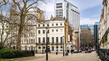 Una calle urbana con edificios históricos, un rascacielos moderno y un cielo despejado.
