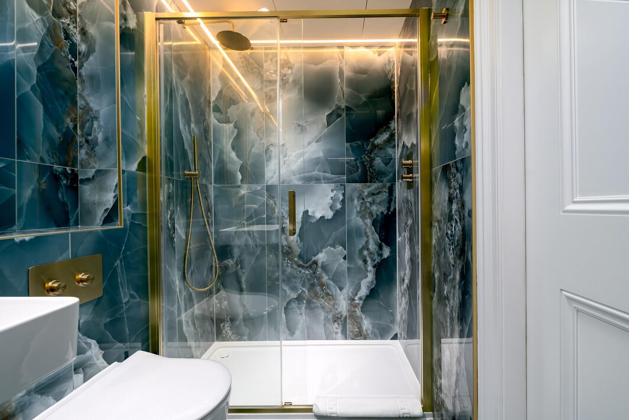 A bathroom with a glass-enclosed shower, marble walls, and a white sink.