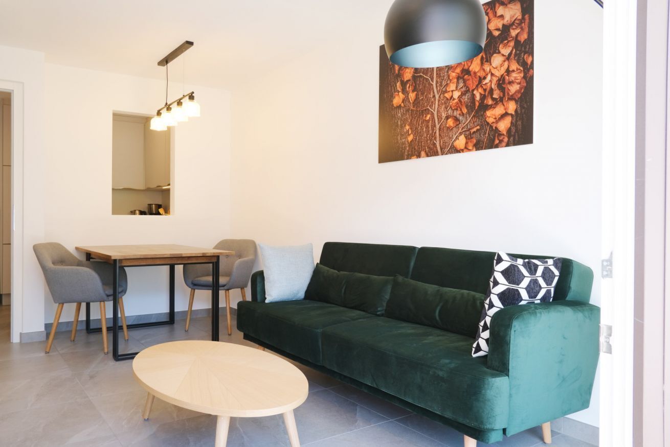 Ein modernes Wohnzimmer mit einem grünen Sofa, einem runden Couchtisch und einem Essbereich mit Tisch und Stühlen.