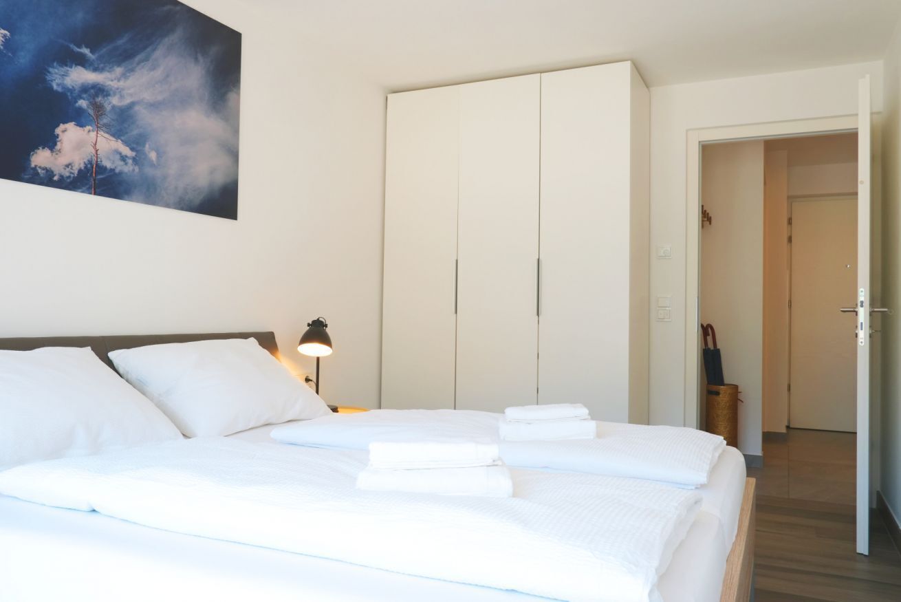 Ein Hotelzimmer mit Bett, Kleiderschrank, Nachttisch mit Lampe und einem Bild an der Wand.