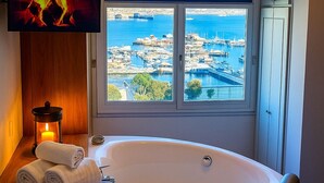 Une salle de bain moderne dotée d’une grande baignoire, d’un téléviseur fixé au-dessus de la baignoire et offrant une vue sur une marina grâce à une grande fenêtre.