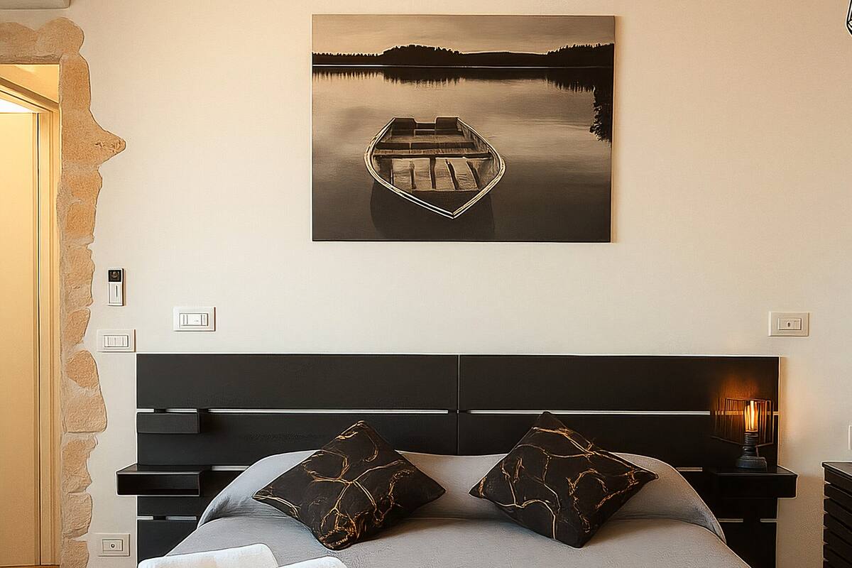 A bedroom with a bed, pillows, a bedside table, and a wall-mounted picture.