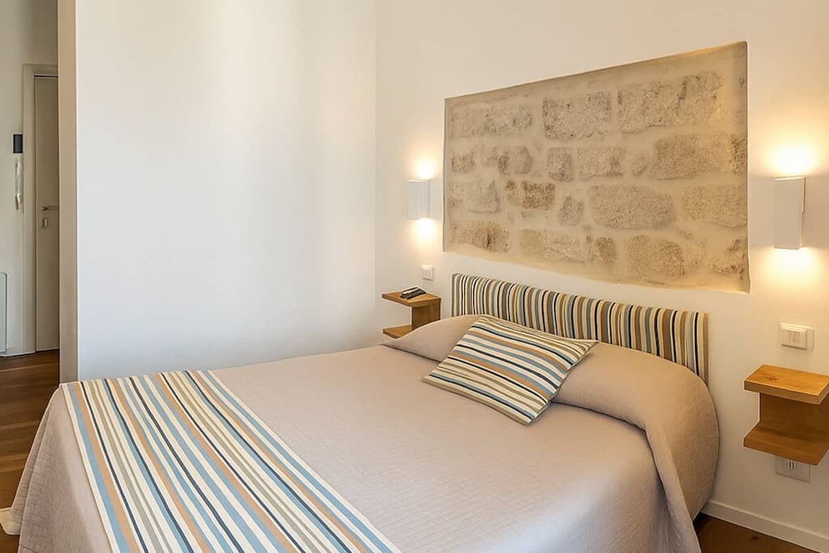 A bedroom with a large bed, striped bedding, a stone wall art piece, and bedside lamps.