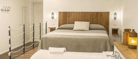 A modern bedroom with a large bathtub, a wooden headboard, and a staircase leading to another room.