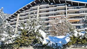 Un edificio a più piani con balconi, circondato da alberi innevati.