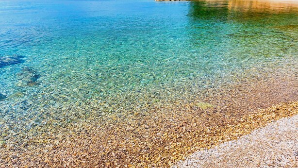 A clear coastal beach with pebbles and a stone wall with trees. - Vacation home Sandra by Interhome (Krk/Krk)