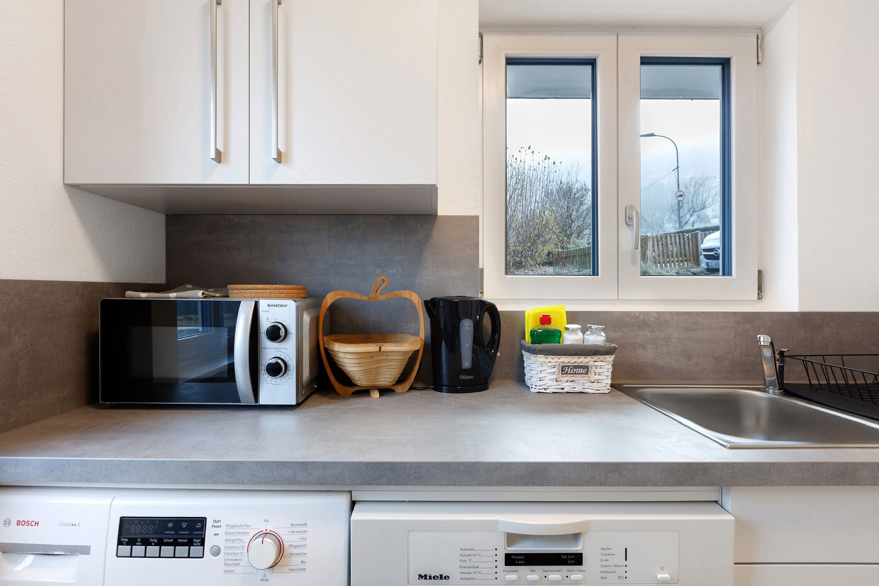 A kitchen with a microwave, toaster, kettle, and a dishwasher.