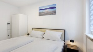 A bedroom with a bed, a nightstand with a lamp, a wardrobe, and a painting on the wall. - Apartment 'Fewo Am Mühlenbach' with Shared Garden and Wi-Fi (Wehr)