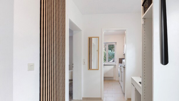 A hallway with a wooden slat wall, a mirror, and a kitchen area visible through an open door. - Apartment 'Fewo Am Mühlenbach' with Shared Garden and Wi-Fi (Wehr)