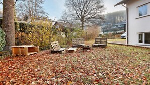 A backyard with a wooden deck, outdoor furniture, and a house in the background. - Apartment 'Fewo Am Mühlenbach' with Shared Garden and Wi-Fi (Wehr)