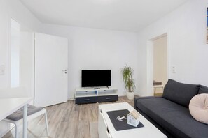 A modern living room with a flat-screen TV, a sofa, a coffee table, and a dining area. - Apartment 'Fewo Am Mühlenbach' with Shared Garden and Wi-Fi (Wehr)