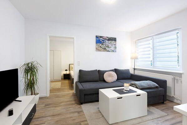 A modern living room with a grey sofa, a white coffee table, a TV, and a plant.